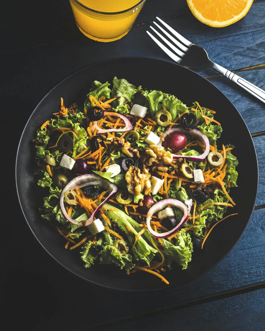 Koyu bir tabakta mor soğanlı ve cevizli yeşil salata